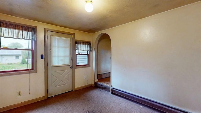 entryway featuring carpet flooring, arched walkways, baseboards, and a baseboard heating unit