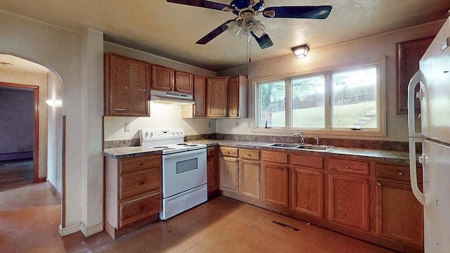 kitchen featuring under cabinet range hood, brown cabinetry, white appliances, ceiling fan, and a sink