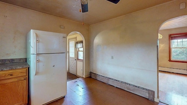 kitchen featuring a baseboard heating unit, freestanding refrigerator, tile patterned floors, ceiling fan, and arched walkways