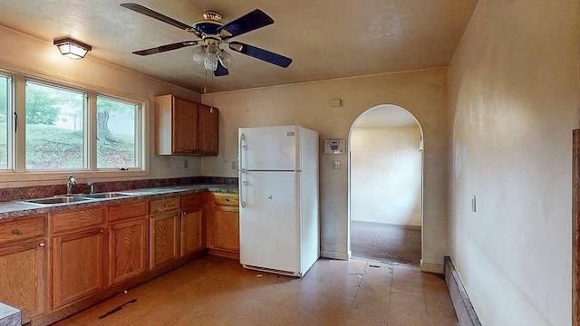 kitchen with a sink, brown cabinetry, freestanding refrigerator, light floors, and arched walkways