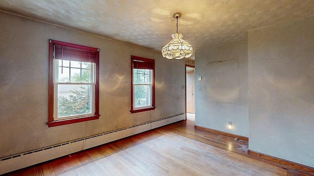 spare room with wood-type flooring, baseboards, a baseboard heating unit, and a notable chandelier