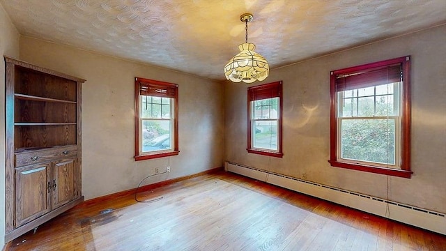 unfurnished room with a chandelier, wood-type flooring, and baseboard heating