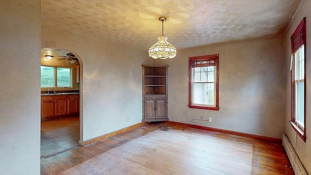 unfurnished dining area with light wood finished floors, baseboards, baseboard heating, and a sink