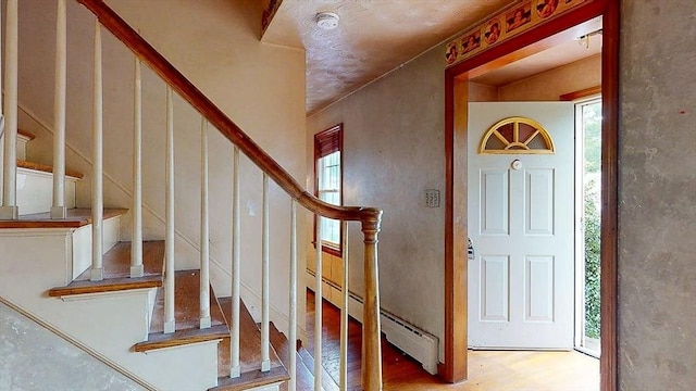 foyer entrance with stairway, baseboard heating, a healthy amount of sunlight, and wood finished floors
