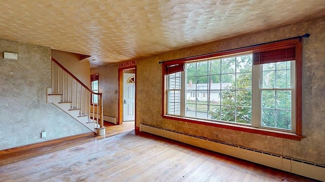 interior space with wood-type flooring, a healthy amount of sunlight, a baseboard heating unit, and a textured ceiling
