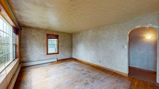 spare room featuring baseboards, baseboard heating, arched walkways, and hardwood / wood-style flooring