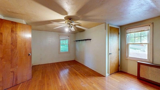 unfurnished bedroom with baseboards, radiator, multiple windows, and hardwood / wood-style flooring