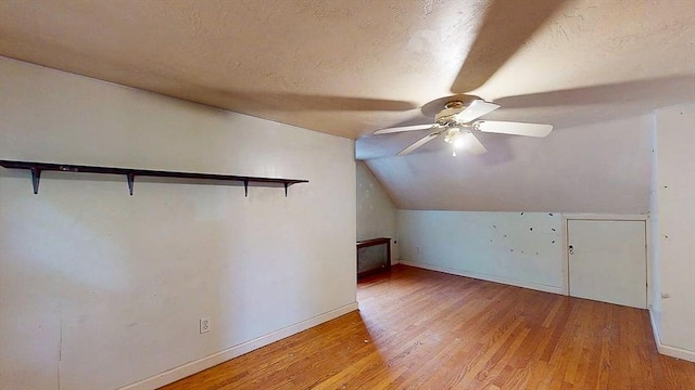 additional living space with lofted ceiling, a textured ceiling, a ceiling fan, baseboards, and light wood-style floors