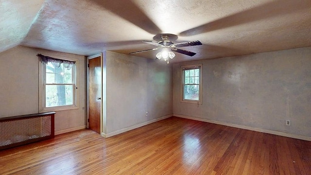 unfurnished room with radiator, wood finished floors, a textured ceiling, a ceiling fan, and baseboards