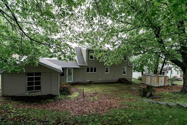 back of house with roof with shingles, a shed, and an outbuilding
