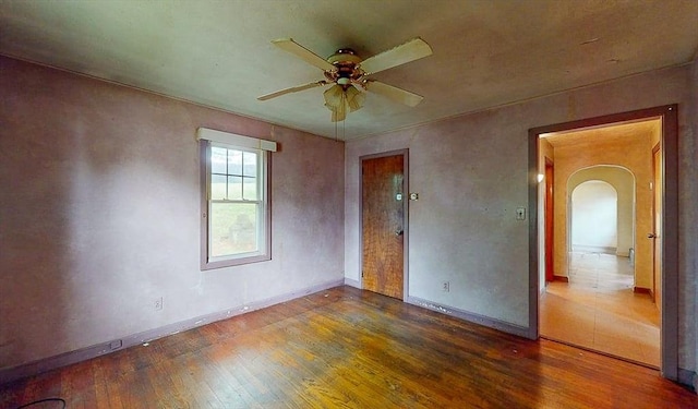 empty room with arched walkways, hardwood / wood-style floors, a ceiling fan, and baseboards