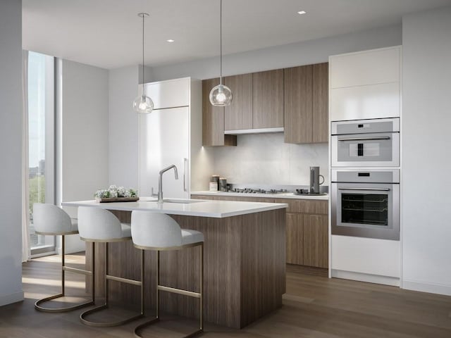 kitchen with a kitchen island with sink, white appliances, a sink, light countertops, and modern cabinets