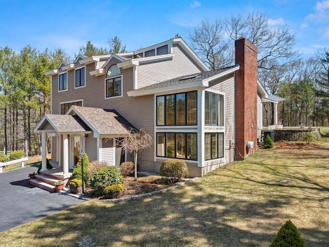 view of front of house featuring a front yard, a shingled roof, and a chimney