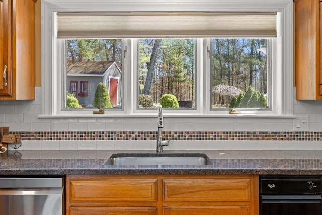 kitchen featuring dark stone countertops, dishwasher, a sink, and backsplash