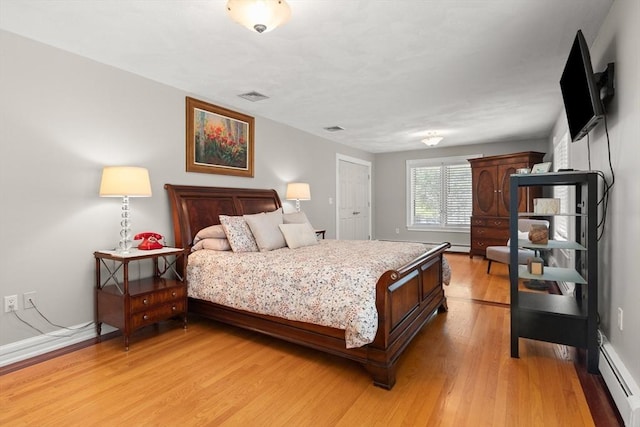 bedroom featuring light wood finished floors, visible vents, a baseboard heating unit, and baseboards