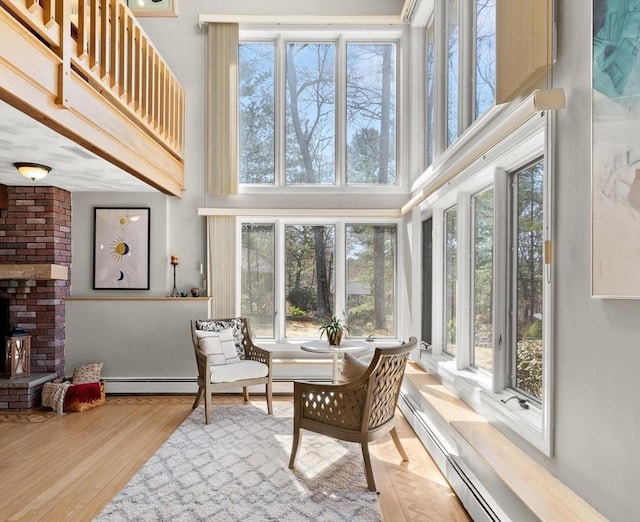 sunroom with a high ceiling, wood finished floors, plenty of natural light, and a baseboard heating unit