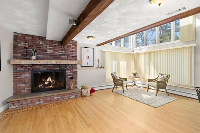 living area with beamed ceiling, visible vents, hardwood / wood-style floors, a brick fireplace, and baseboards