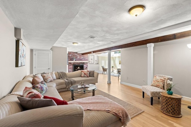 living room with a fireplace, light wood-style flooring, a textured ceiling, visible vents, and baseboards