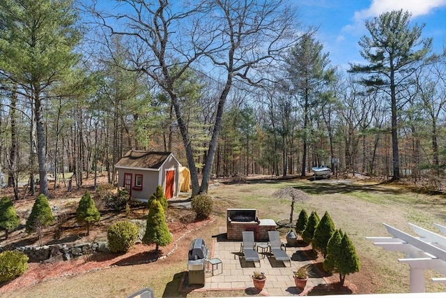 view of yard featuring a wooded view, a patio area, and an outbuilding