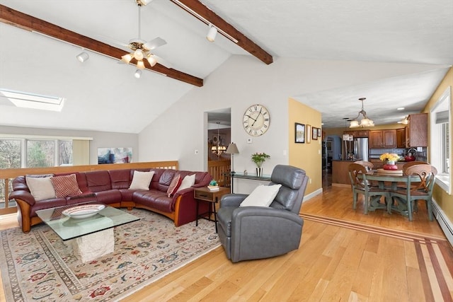 living area featuring baseboards, track lighting, light wood-style floors, lofted ceiling with skylight, and ceiling fan with notable chandelier