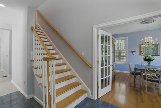 stairway with wood finished floors, a chandelier, and baseboards