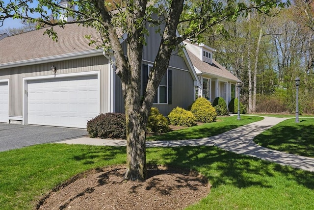 view of side of property featuring a lawn, roof with shingles, a garage, and aphalt driveway
