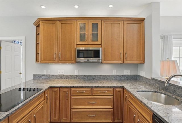 kitchen featuring a sink, open shelves, brown cabinetry, black appliances, and light stone counters