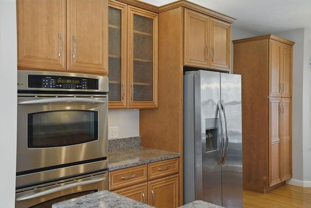 kitchen featuring stone countertops, brown cabinetry, stainless steel appliances, and light wood-style floors