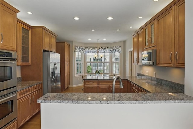 kitchen with a peninsula, brown cabinets, recessed lighting, and appliances with stainless steel finishes