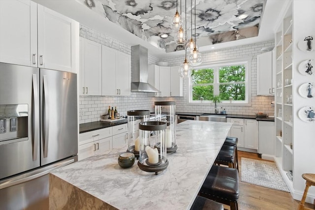 kitchen with stainless steel appliances, wall chimney exhaust hood, a sink, tasteful backsplash, and white cabinets