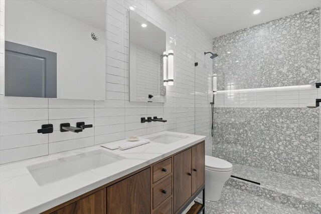 full bath with tile walls, a walk in shower, toilet, double vanity, and recessed lighting