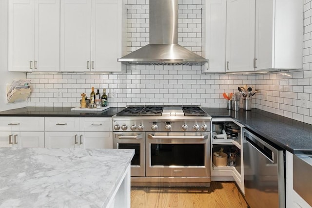kitchen with appliances with stainless steel finishes, wall chimney exhaust hood, white cabinets, tasteful backsplash, and light wood-style floors
