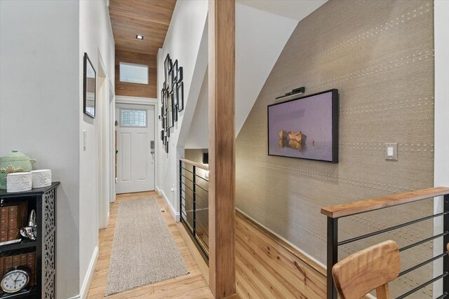 corridor with wood finished floors, baseboards, an accent wall, and stairway