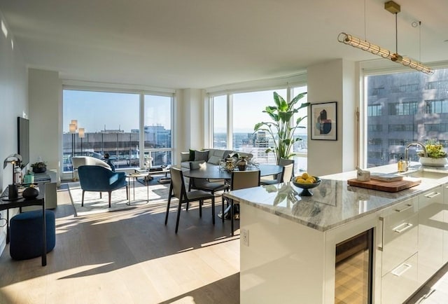 kitchen with light stone countertops, decorative light fixtures, a wall of windows, white cabinets, and wine cooler