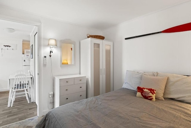 bedroom with ornamental molding, freestanding refrigerator, and wood finished floors