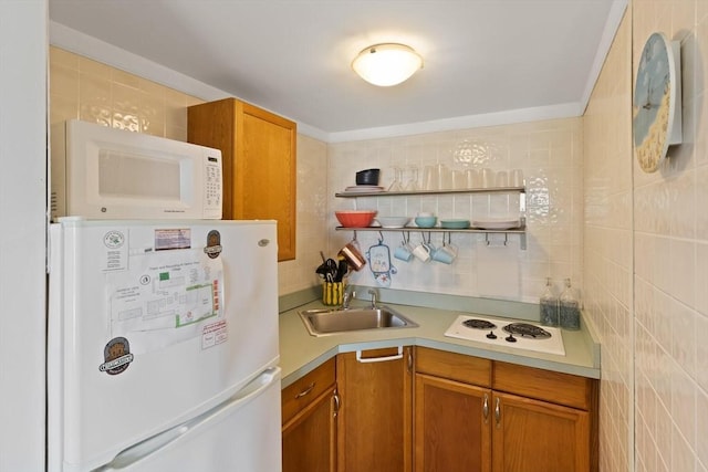 kitchen with brown cabinetry, white appliances, a sink, and tile walls