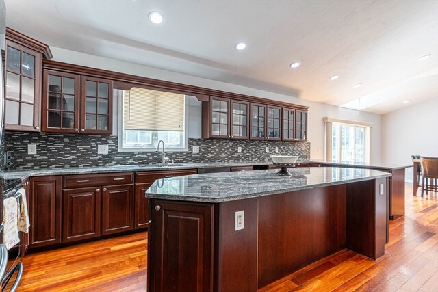 kitchen featuring dark stone counters, decorative backsplash, stove, a kitchen island, and light hardwood / wood-style flooring