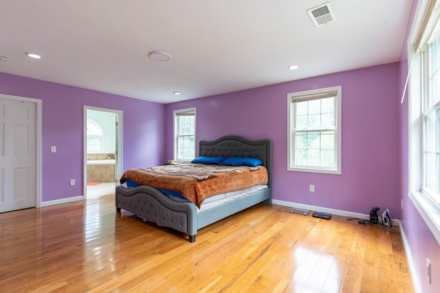 bedroom featuring multiple windows, ensuite bath, and light wood-type flooring