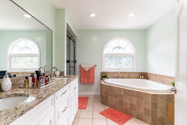 bathroom featuring a relaxing tiled tub, tile patterned floors, double vanity, and a healthy amount of sunlight