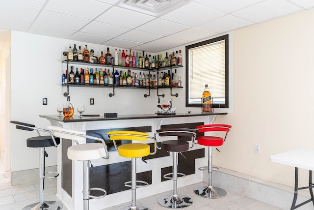 bar with a paneled ceiling and light tile patterned floors