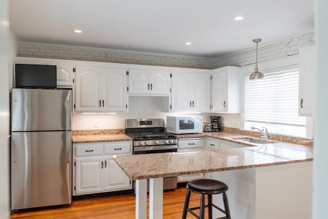 19 Center St, Weymouth, MA 02189 - kitchen with appliances with stainless steel finishes, white cabinets, light stone counters, light wood-type flooring, and a breakfast bar area