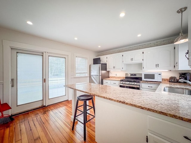 19 Center St, Weymouth, MA 02189 - kitchen featuring appliances with stainless steel finishes, a peninsula, white cabinets, light stone countertops, and light wood-type flooring