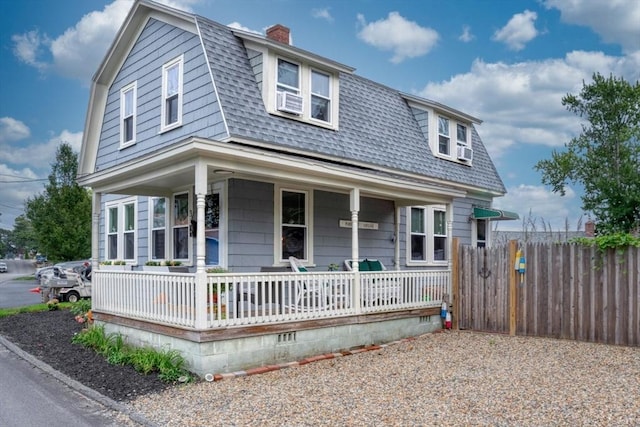 colonial inspired home with cooling unit, covered porch, fence, a gambrel roof, and roof with shingles