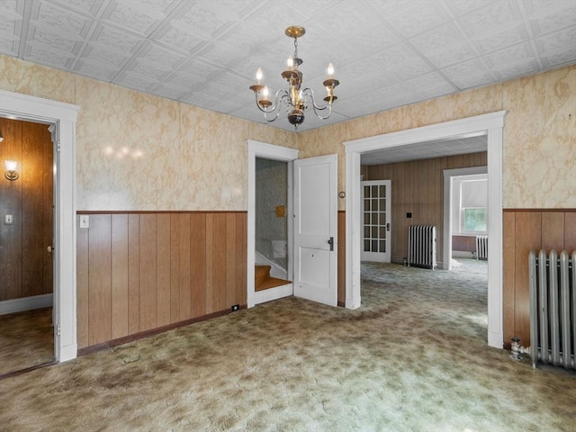 unfurnished dining area featuring radiator heating unit, a chandelier, wooden walls, carpet floors, and wainscoting