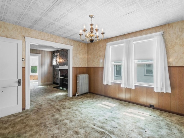 unfurnished dining area with radiator heating unit, a chandelier, a fireplace, a wainscoted wall, and wooden walls