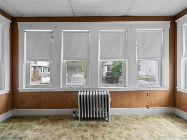 spare room featuring radiator heating unit, carpet floors, plenty of natural light, and wood walls