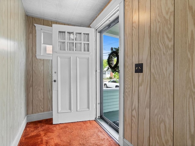 doorway to outside with carpet floors, wooden walls, and baseboards