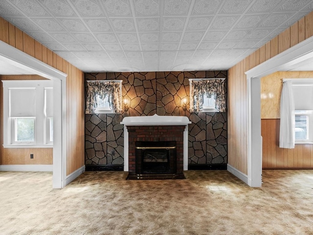 unfurnished living room with baseboards, carpet floors, plenty of natural light, wooden walls, and an ornate ceiling