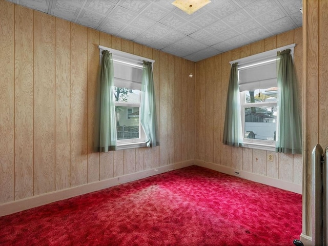 unfurnished room featuring carpet floors, baseboards, wood walls, and an ornate ceiling