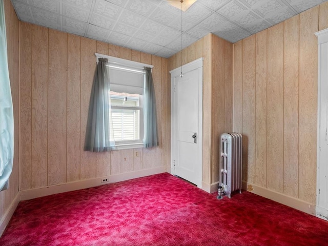 carpeted empty room with radiator, wood walls, baseboards, and an ornate ceiling